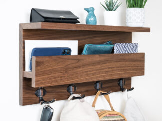 A modern wooden shelf made of solid walnut, with a clear lacquer finish that highlights its natural wood grain. The shelf features a 2-inch slotted shelf for storage of small items like mail, phone, and wallet, and a 4-inch shelf for storing hats, gloves, and purses. The shelf also has four oil brushed double hooks for storing coats, outerwear, and bags